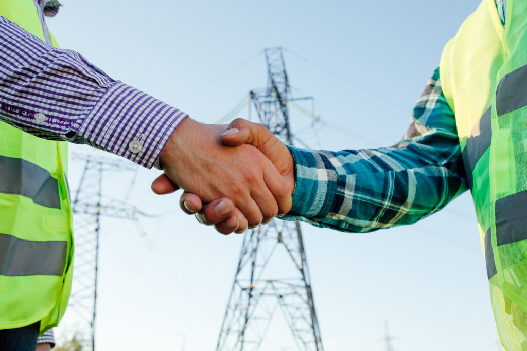 engineers shaking hands against high voltage tower